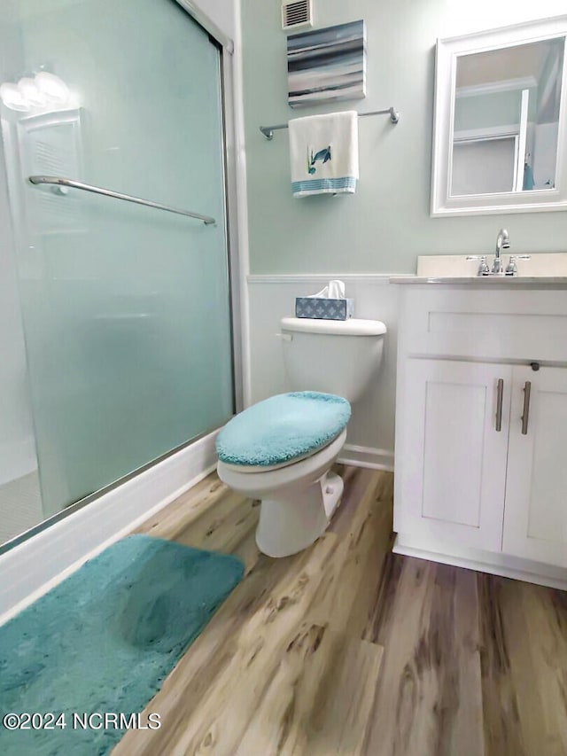 bathroom with wood-type flooring, a shower with shower door, vanity, and toilet