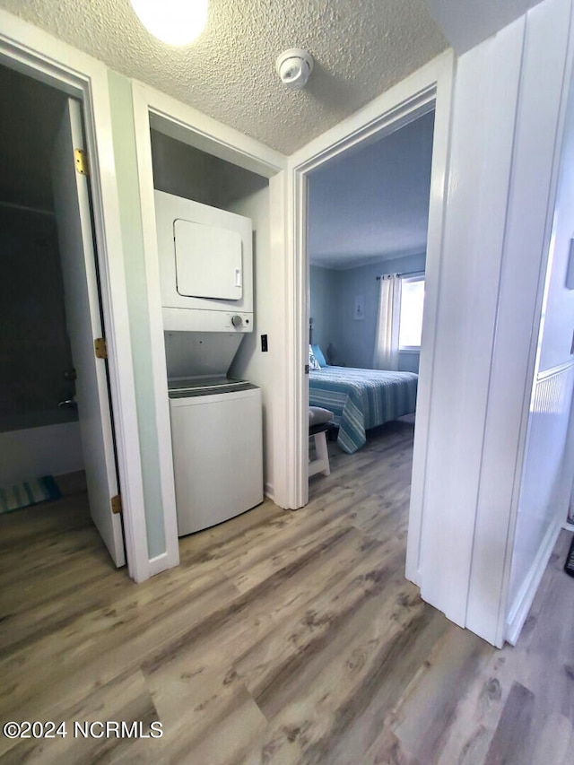 laundry room with a textured ceiling, hardwood / wood-style floors, and stacked washer and dryer