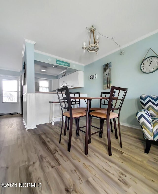 dining area with wood-type flooring, an inviting chandelier, and crown molding