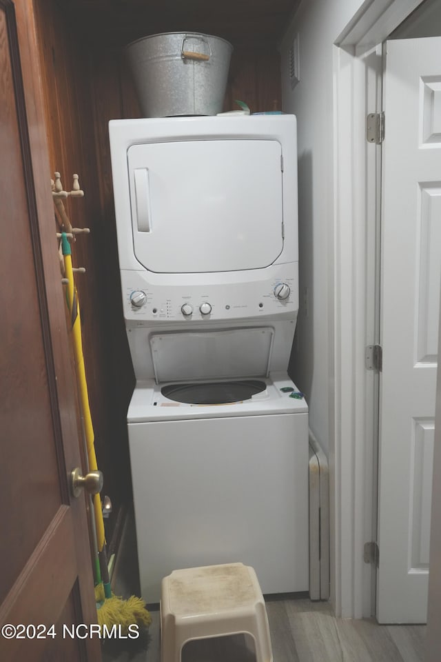 laundry area featuring wood-type flooring and stacked washer and clothes dryer