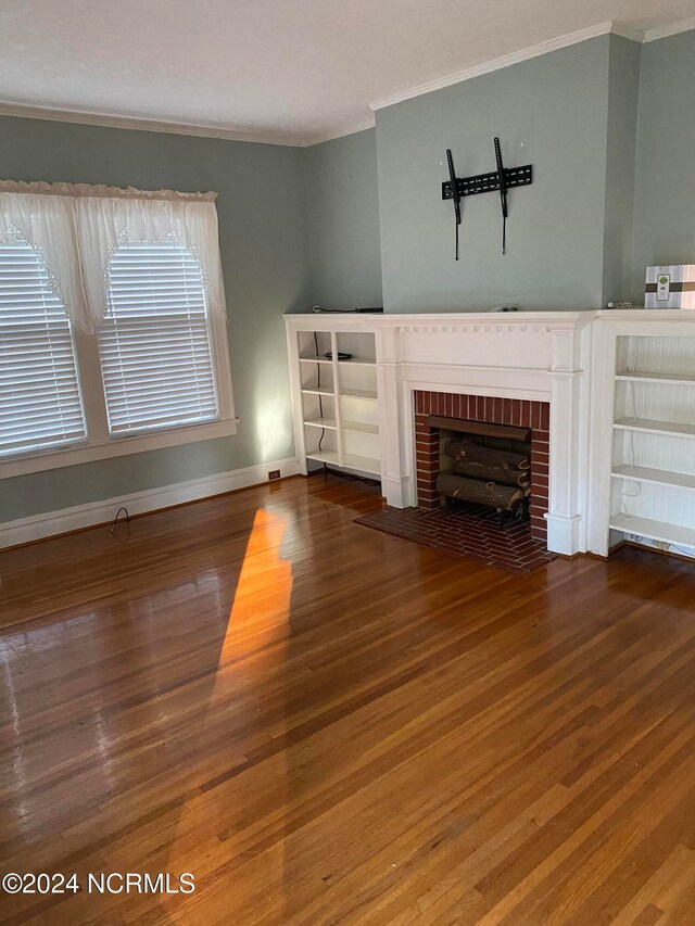 unfurnished living room featuring hardwood / wood-style flooring, crown molding, and a brick fireplace