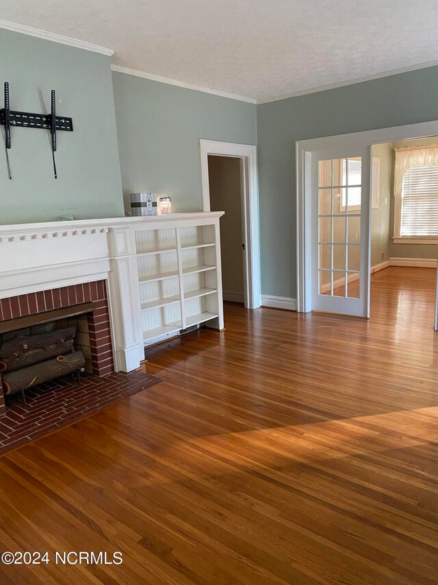 unfurnished living room featuring wood-type flooring, a textured ceiling, a brick fireplace, and ornamental molding