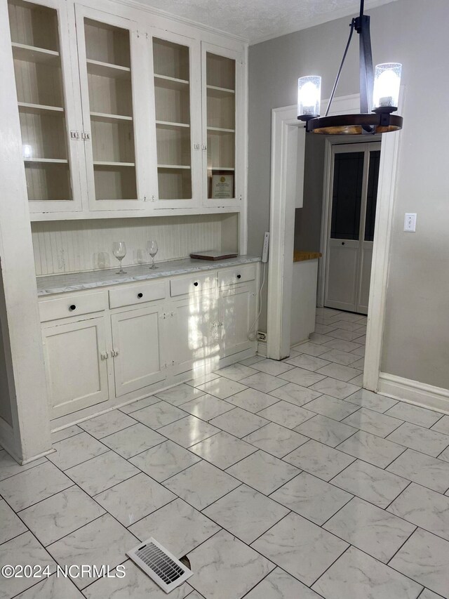 interior space featuring white cabinetry, decorative light fixtures, a chandelier, and a textured ceiling