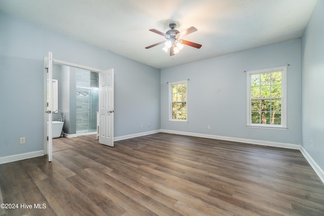 unfurnished bedroom featuring connected bathroom, dark wood-type flooring, multiple windows, and ceiling fan