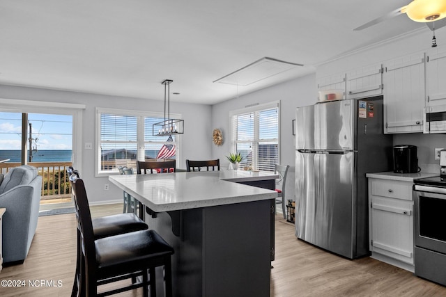 kitchen featuring white cabinetry, stainless steel appliances, pendant lighting, a water view, and a breakfast bar area