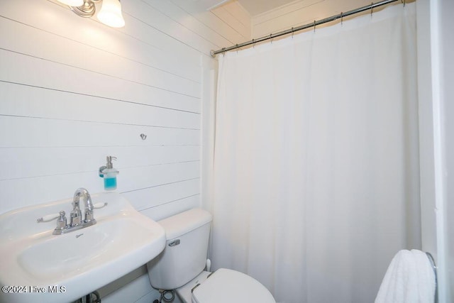 full bath with a sink, toilet, a shower with curtain, and wood walls