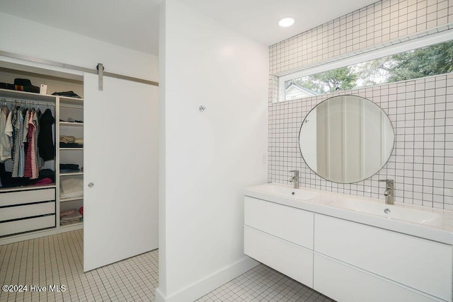 full bath with tile walls, a spacious closet, double vanity, and tile patterned flooring
