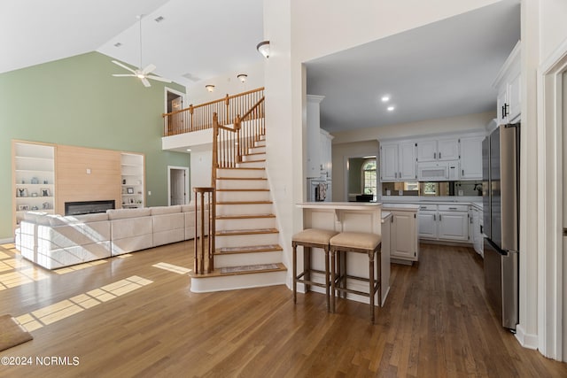 kitchen with dark hardwood / wood-style floors, a kitchen breakfast bar, stainless steel fridge, white cabinetry, and ceiling fan