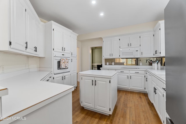 kitchen featuring white cabinetry, a center island, light wood-type flooring, and white appliances