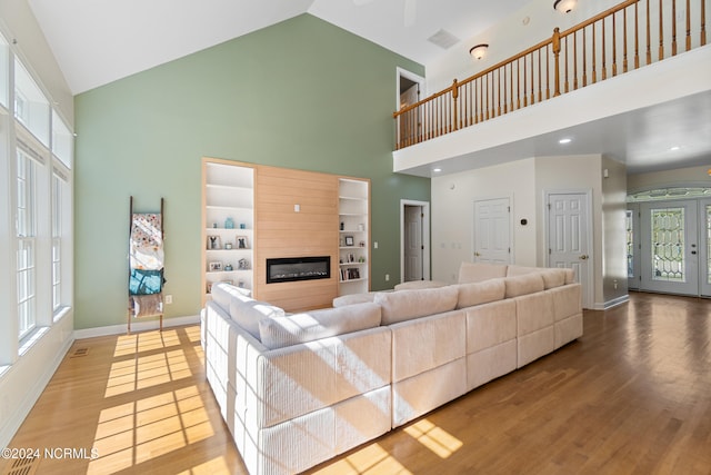 living room featuring built in features, light wood-type flooring, and high vaulted ceiling