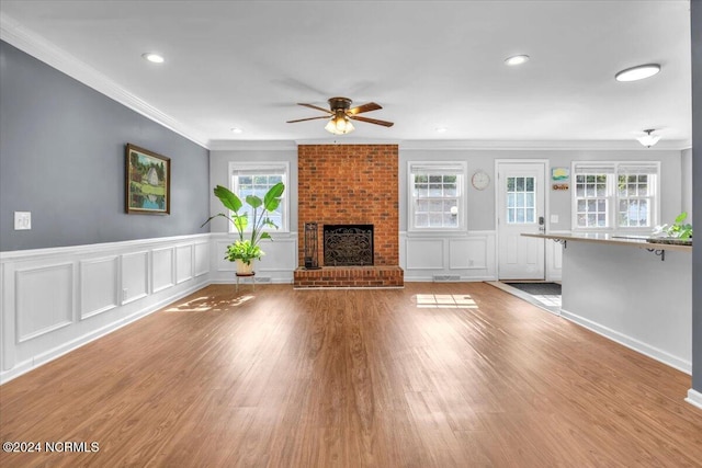 unfurnished living room featuring ceiling fan, a healthy amount of sunlight, ornamental molding, and a brick fireplace