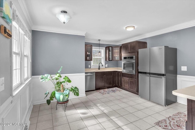 kitchen with appliances with stainless steel finishes, crown molding, sink, light tile patterned floors, and decorative light fixtures