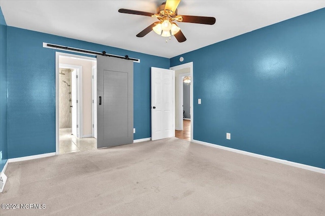 unfurnished bedroom featuring a barn door, light colored carpet, and ceiling fan