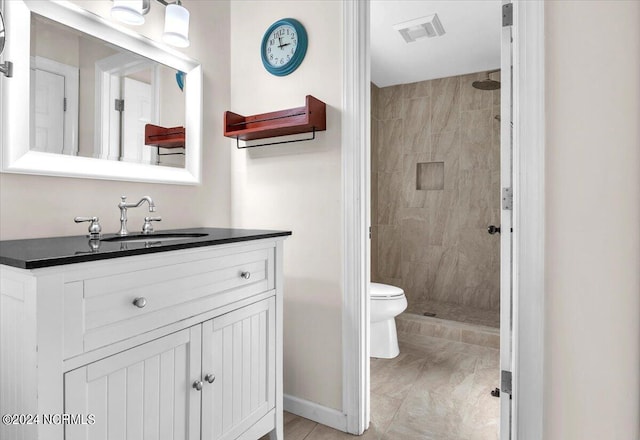 bathroom with a tile shower, vanity, and toilet