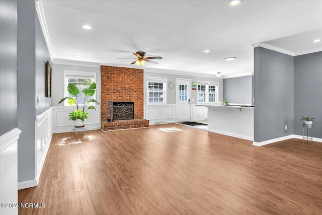 unfurnished living room featuring ceiling fan, wood-type flooring, crown molding, and a brick fireplace