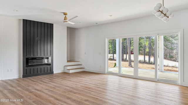 spare room with a fireplace, light wood-type flooring, and ceiling fan with notable chandelier