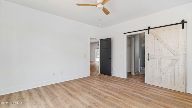 unfurnished bedroom with light hardwood / wood-style flooring, ceiling fan, a spacious closet, and a barn door