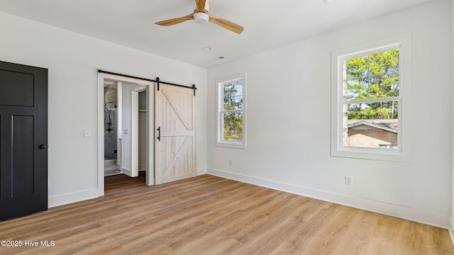 unfurnished bedroom featuring light wood-type flooring, ceiling fan, and a barn door