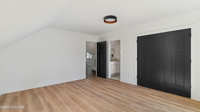 unfurnished bedroom with light hardwood / wood-style floors, vaulted ceiling, and connected bathroom