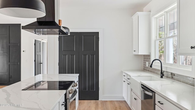 kitchen with white cabinetry, appliances with stainless steel finishes, light stone counters, and range hood