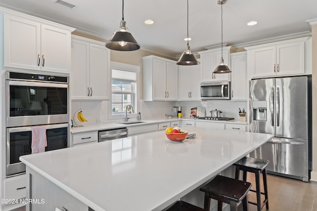 kitchen with white cabinets, appliances with stainless steel finishes, decorative light fixtures, and a center island