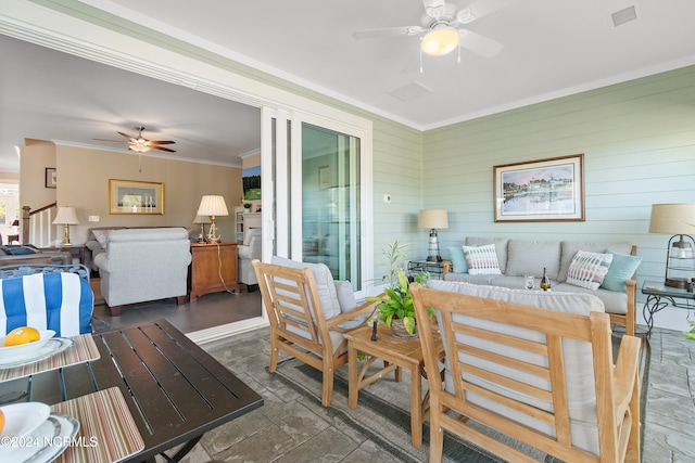 living room featuring wood walls, ceiling fan, and crown molding