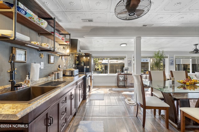 kitchen with wall chimney range hood, hardwood / wood-style floors, sink, dark brown cabinetry, and ceiling fan