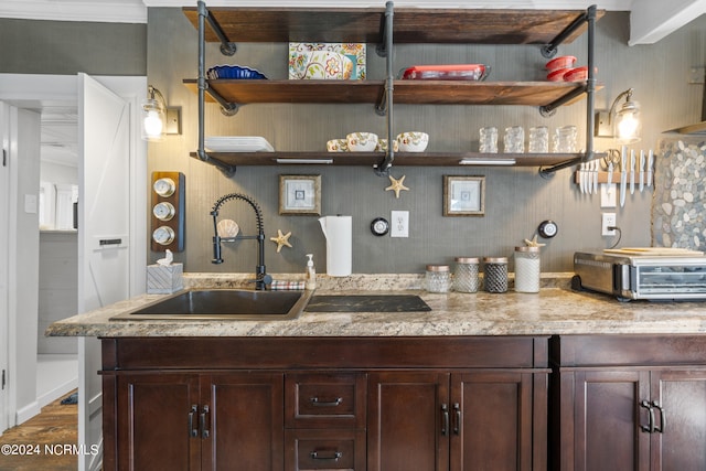 kitchen with hardwood / wood-style floors, light stone countertops, crown molding, dark brown cabinetry, and sink