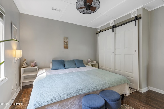 bedroom featuring crown molding, dark hardwood / wood-style floors, multiple windows, and a barn door