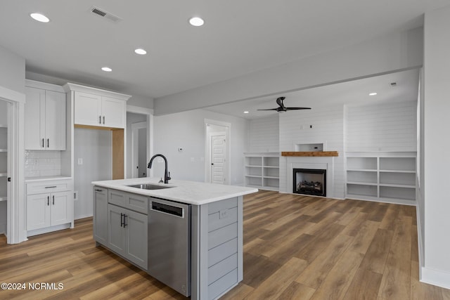 kitchen with white cabinets, a kitchen island with sink, stainless steel dishwasher, a fireplace, and sink