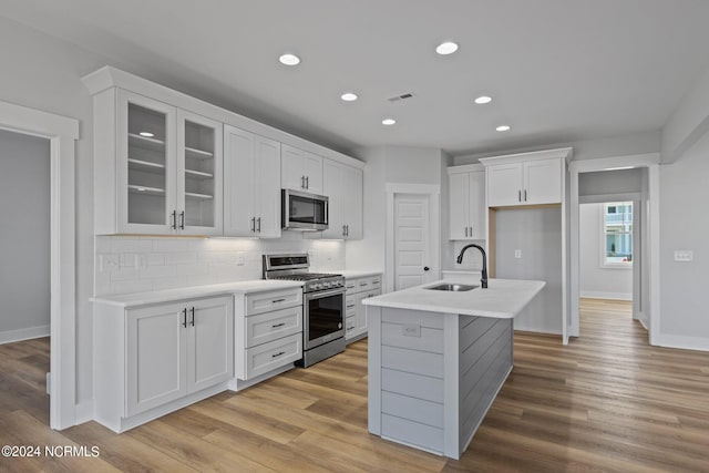 kitchen with sink, white cabinetry, light hardwood / wood-style floors, stainless steel appliances, and a kitchen island with sink