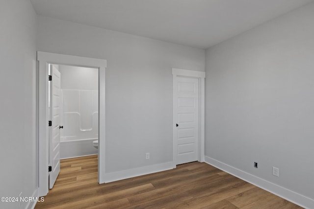 unfurnished bedroom with ensuite bath and hardwood / wood-style flooring