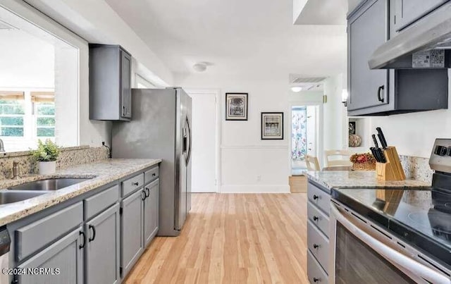 kitchen featuring light wood-type flooring, light stone counters, sink, and stainless steel appliances