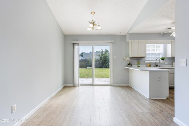 kitchen with kitchen peninsula, hanging light fixtures, ceiling fan with notable chandelier, light hardwood / wood-style floors, and sink