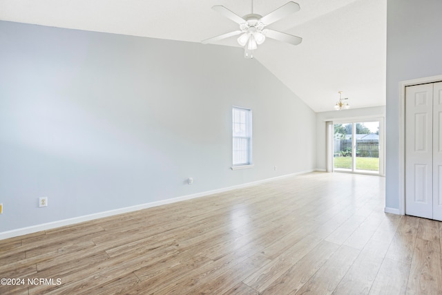 spare room featuring light hardwood / wood-style floors, high vaulted ceiling, and ceiling fan with notable chandelier