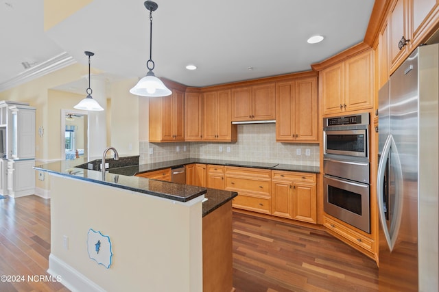 kitchen with ornamental molding, kitchen peninsula, stainless steel appliances, dark hardwood / wood-style floors, and dark stone countertops