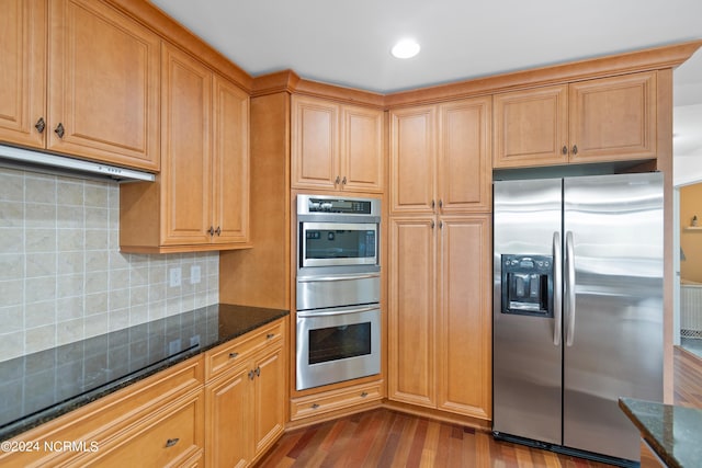 kitchen featuring tasteful backsplash, wood-type flooring, dark stone countertops, and appliances with stainless steel finishes