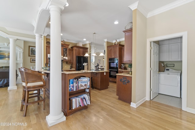 kitchen with washer / dryer, black appliances, hanging light fixtures, and light hardwood / wood-style floors