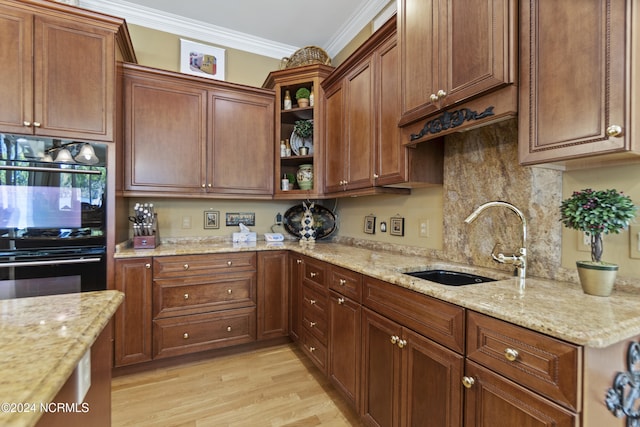 kitchen with sink, double oven, light stone counters, crown molding, and light hardwood / wood-style flooring