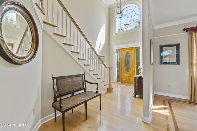 foyer entrance featuring a chandelier, crown molding, light wood-type flooring, and a high ceiling