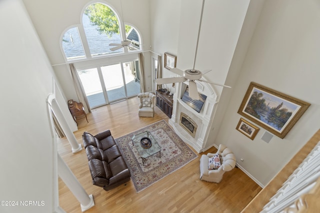 living room with ceiling fan, wood-type flooring, a high ceiling, and a fireplace