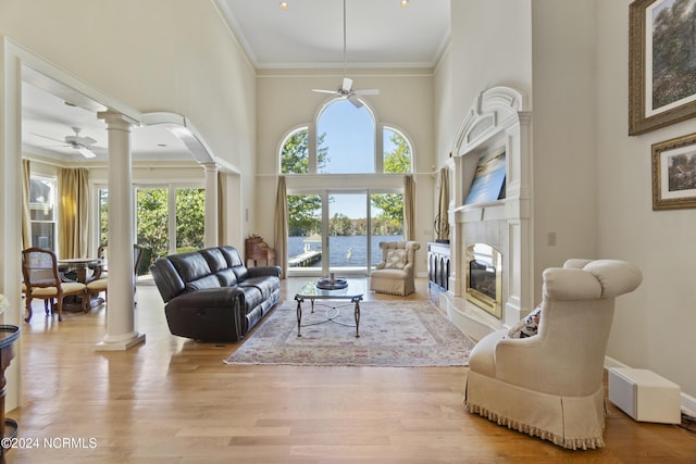 living room with ceiling fan, decorative columns, a towering ceiling, crown molding, and light hardwood / wood-style floors