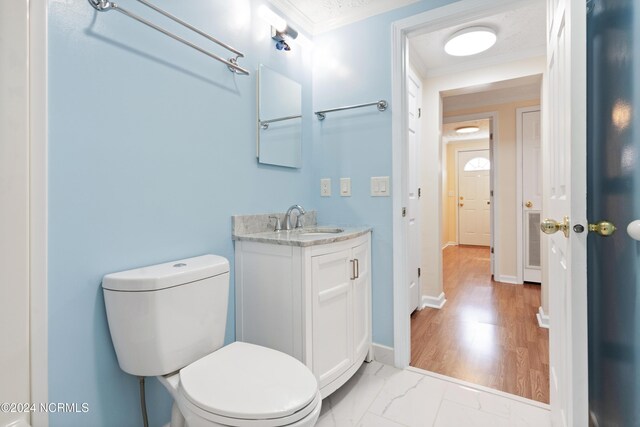 half bathroom with vanity, toilet, ornamental molding, and marble finish floor