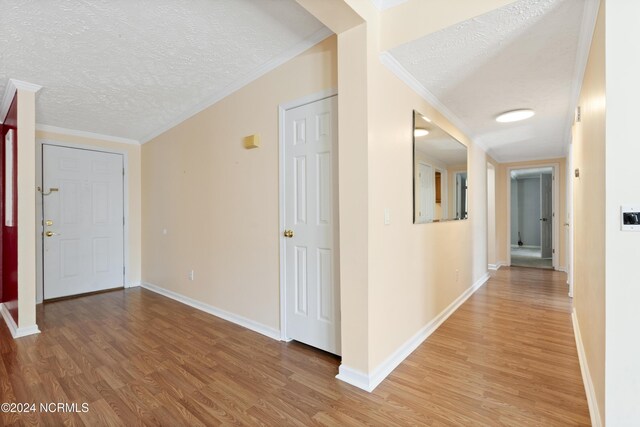 corridor featuring baseboards, a textured ceiling, and light wood finished floors