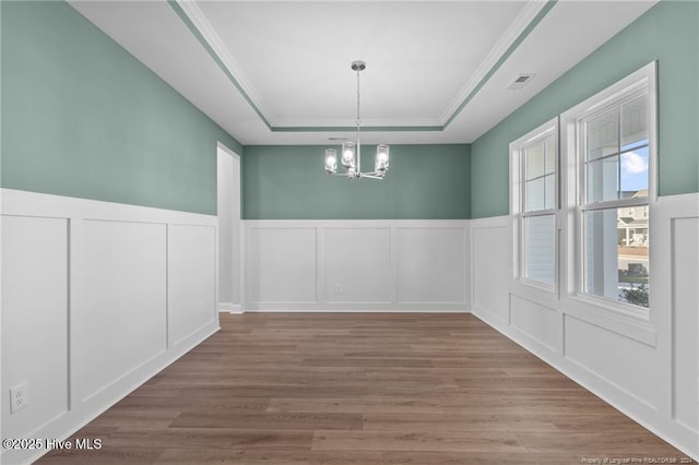 unfurnished dining area featuring hardwood / wood-style floors, a raised ceiling, crown molding, and a chandelier