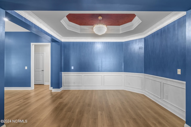 empty room featuring wood-type flooring, crown molding, a tray ceiling, and a notable chandelier