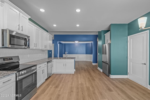 kitchen with light stone countertops, stainless steel appliances, kitchen peninsula, white cabinetry, and light hardwood / wood-style flooring