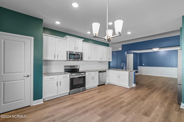 kitchen with light wood-type flooring, stainless steel appliances, white cabinets, kitchen peninsula, and decorative light fixtures