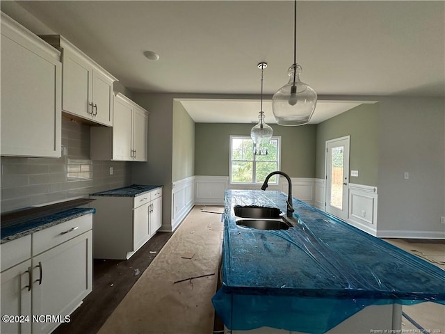 kitchen with tasteful backsplash, a center island with sink, hanging light fixtures, dark wood-type flooring, and sink