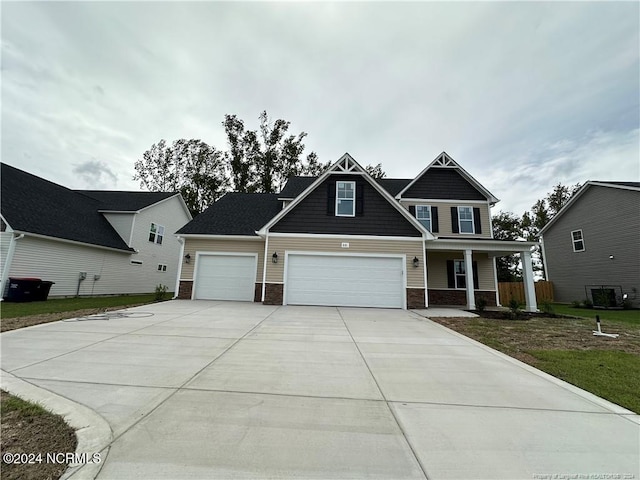 craftsman-style house with central air condition unit, covered porch, a front lawn, and a garage